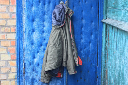 one winter green jacket hanging on blue door and brown brick wall on winter streetの写真素材
