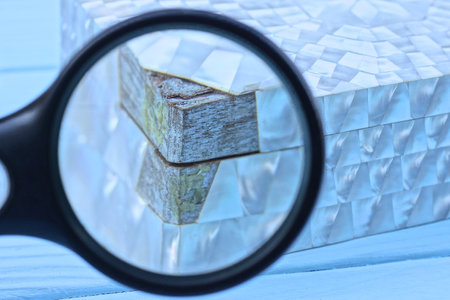 one black magnifying glass magnifies part of a white box with a peeling gray wooden board on the...