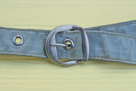 part of an old belt made of gray dirty fabric with a white metal buckle lies on the yellow wooden...