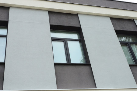 a row of three black windows on a gray concrete brown wall of a big building on the street