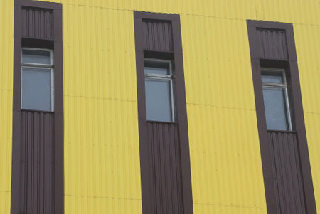 a row of three windows on a metal yellow wall of an industrial building on a city street