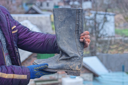 man's hands holding one old gray tarpaulin army boot on autumn street
