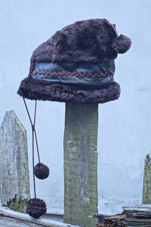 one childrens brown winter hat made of leather and fur with pompoms hanging on a wooden fence board...