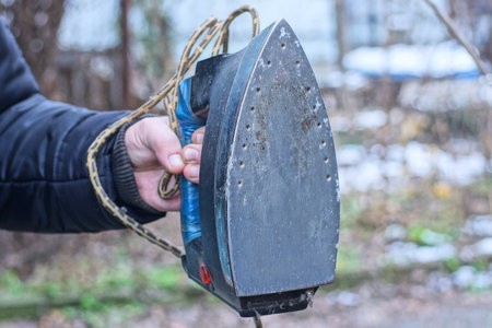 hand holding one old black gray big electric iron on autumn streetの写真素材