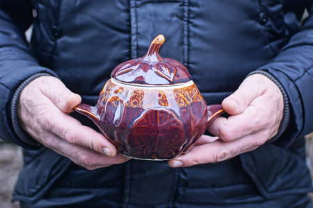 hand holds one brown one ceramic pot covered with a lid on an autumn streetの写真素材