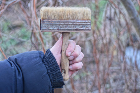 hand in black clothes holding one big gray brown wooden paint brush on autumn streetの写真素材
