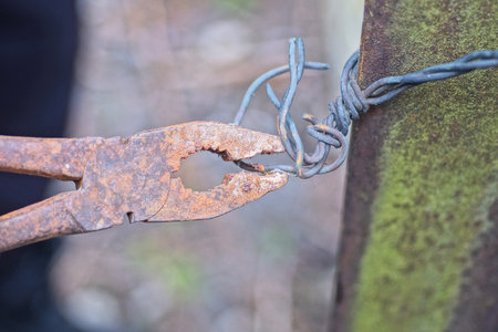 one brown old rusty iron pliers twisting black metal wire on fence post on rural streetの写真素材