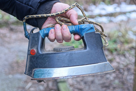 hand holding one old black gray big electric iron on autumn streetの写真素材