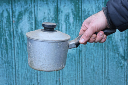 hand holds one gray cast iron saucepan with a black handle against a green backgroundの写真素材