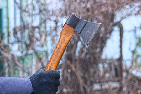 one hand in a black glove holds a small gray ax with a brown wooden handle on an autumn streetの写真素材
