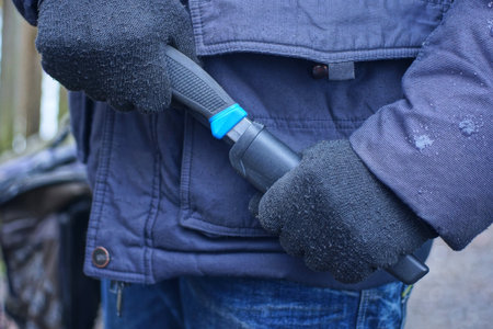 man's hands in black gloves holding a knife and putting it in a plastic case on an autumn streetの写真素材