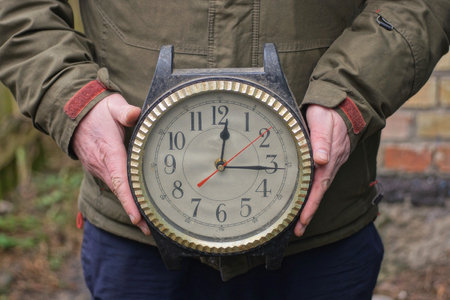 a man in green clothes holds in his hands one large old plastic brown black winged clock