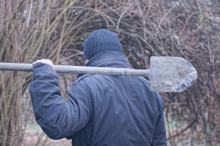 holds a long gray dirty shovel in his hand on his shoulder on an autumn street