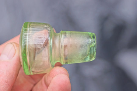hand holding one old green glass stopper from decanter on gray background