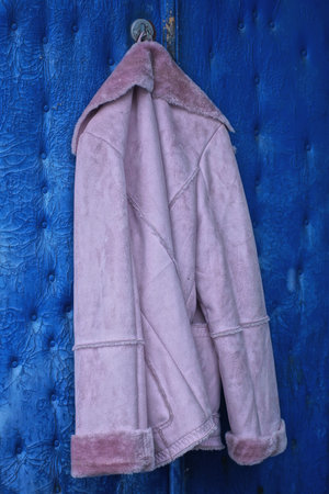 one suede winter pink coat with fur collar hanging on blue door