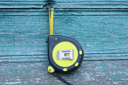 one plastic yellow black construction tape measure lies on a green wooden table