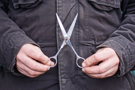 hands of man in black clothes holding one old metal gray big scissors on autumn street