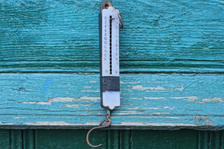 one white old plastic canter scale hanging on green wooden wall on summer street