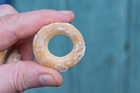 fingers on hand holding one small brown donut on green background