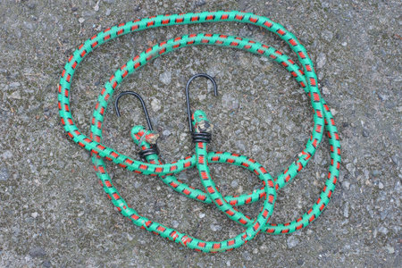 one black with green spots a fastening cable made of fabric and rubber with metal hooks lies on a...