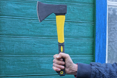 one male worker in blue clothes holds a black yellow ax in his hand on the street against the...
