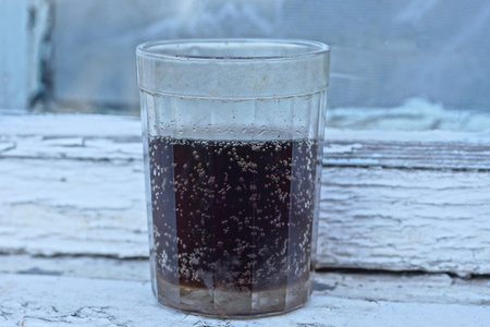 one glass cup with black drink and white foam stands on a white wooden table