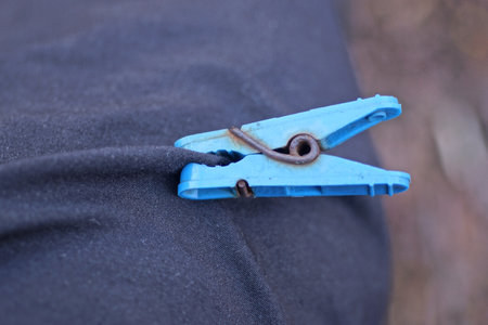 one old blue plastic clothespin pinches black fabric on clothes