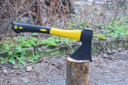 one black yellow big ax sticks out in a brown log on gray asphalt