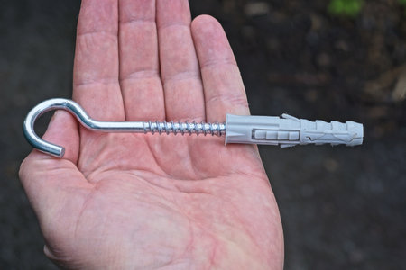 one gray long metal screw hook lies on the palm of the hand