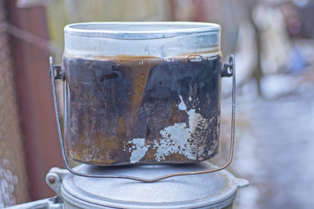 one old closed worn army aluminum pot saucepan stands on a black table on a summer streetの写真素材
