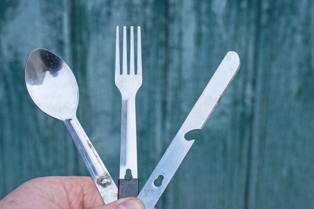 hand holding old set of knife fork and spoon against green wallの写真素材