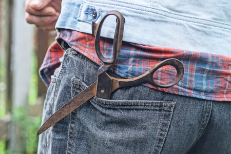 one big old iron brown rusty scissors lies in the pocket of gray denim pants on a manの写真素材
