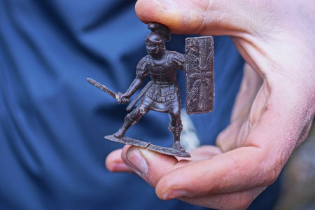 one small old plastic brown toy roman legionnaire stands on the palm on the hand on the summer streetの写真素材