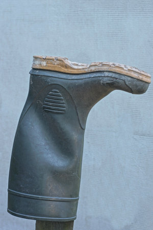 one big rubber boot hangs on a pole against a gray wall on a summer street