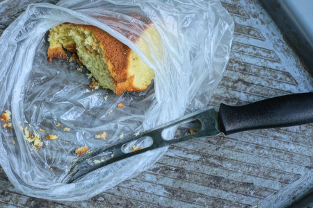 a piece of large brown cake and knife lies on a gray table in white cellophane