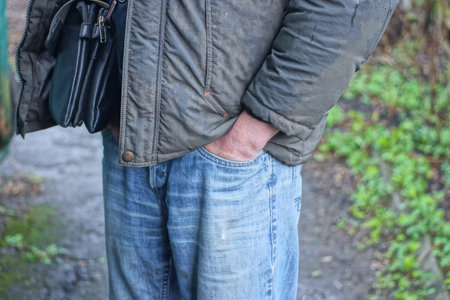 hand of a man in a gray jacket tucked into the pocket of a blue jeans on an autumn streetの写真素材