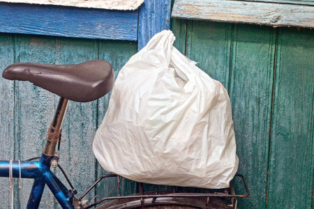 one big white full plastic bag stands on a bicycle rack near a green wall on a summer street