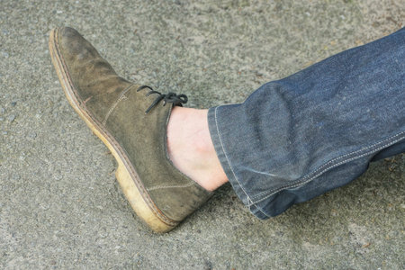 one leg of a man in a gray suede boot on asphalt on the street