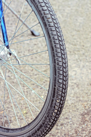 part of a wheel made of gray black rubber tire and metal spokes on a bike in the street