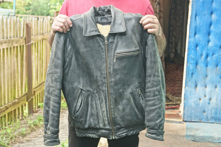 hands of man in red clothes holding old black leather jacket with furの写真素材