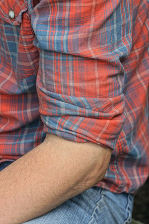 one hand of a man with a rolled up sleeve of a shirt on a summer street