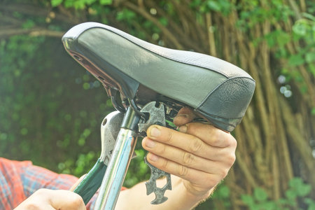 man hand holding black gray bicycle leather saddle with open-end wrench over bicycleの写真素材
