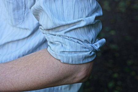 one hand of a man with a white rolled up sleeve of a shirt on a summer streetの写真素材