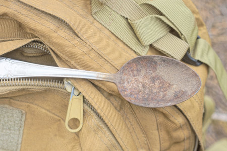one old gray rusty metal spoon lies on in pocket brown fabric backpack in the streetの写真素材