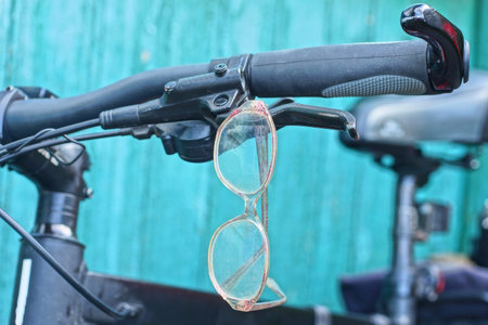 one old gray glasses hangs on the black handlebar of a sports bike near a green wall
