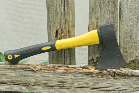 one big ax with black yellow handle lies on gray wooden board of fence on rural street