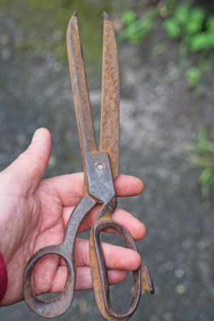 one brown rusty iron old scissors lies on the fingers on the hand in the streetの写真素材