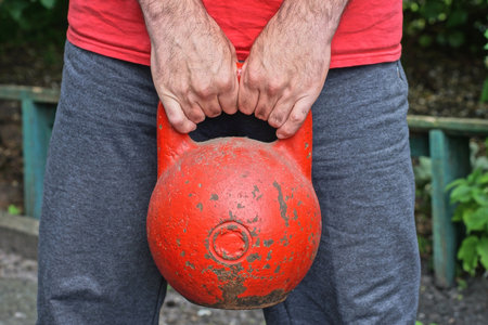 hands of one male athlete lifting one big old red iron sports weight on summer streetの写真素材