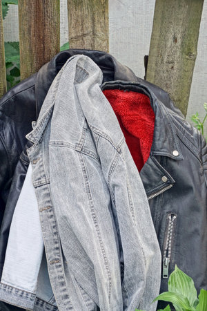 three old black leather jackets and a gray cotton one stand on the ground among green vegetation...