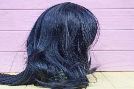 one wig with long black hair stands on a yellow table near a pink wallの写真素材